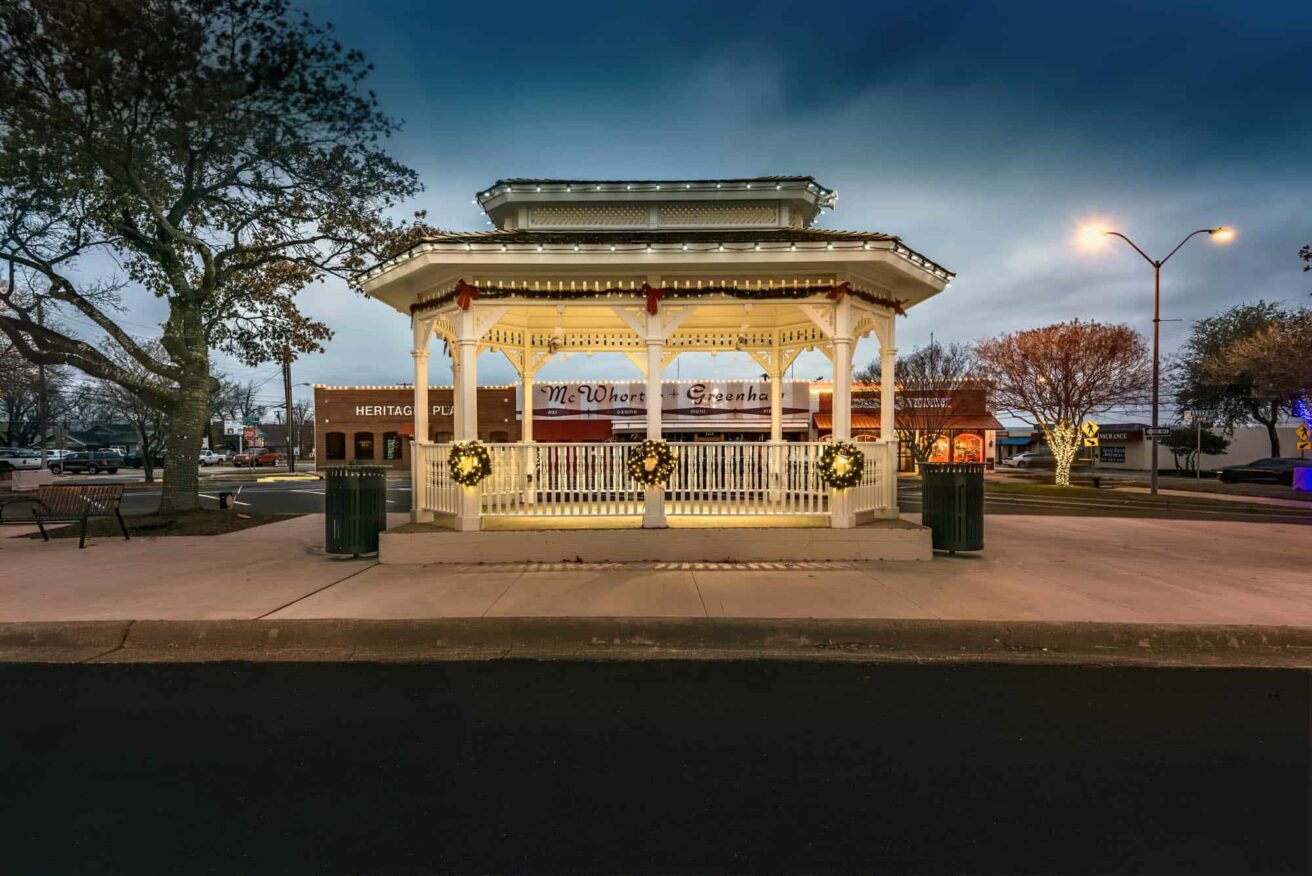 A gazebo sits in the middle of a street at night.