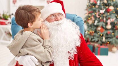 A boy is kissing santa claus in front of a christmas tree.