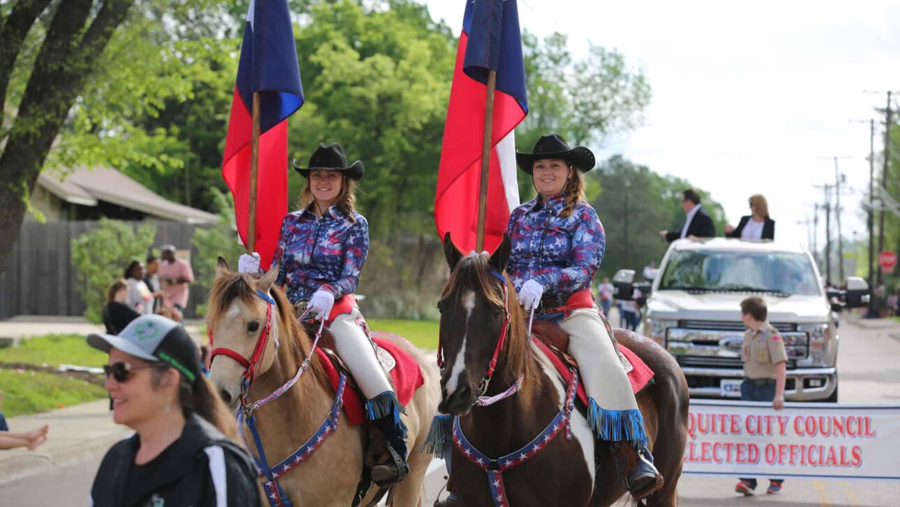 Two cowgirls riding horses in a parade.