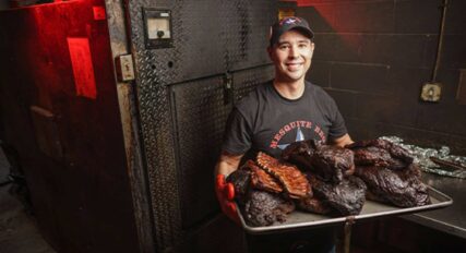 A man holding a tray of ribs in front of an oven.