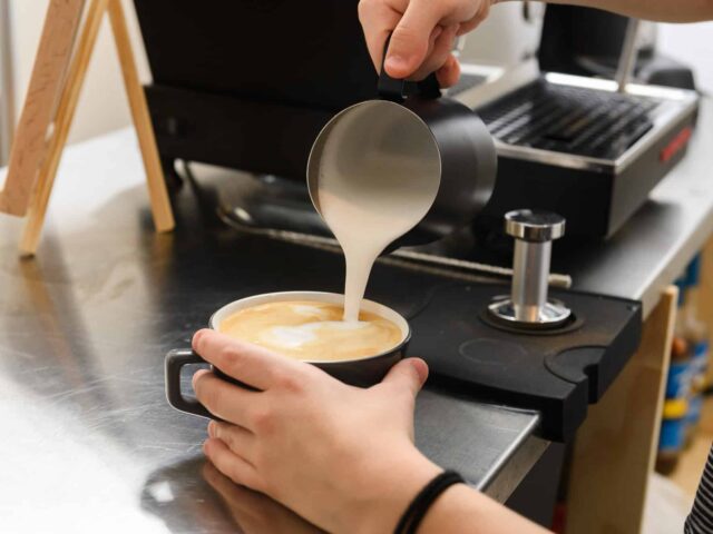 A person pouring milk into a cup of coffee.