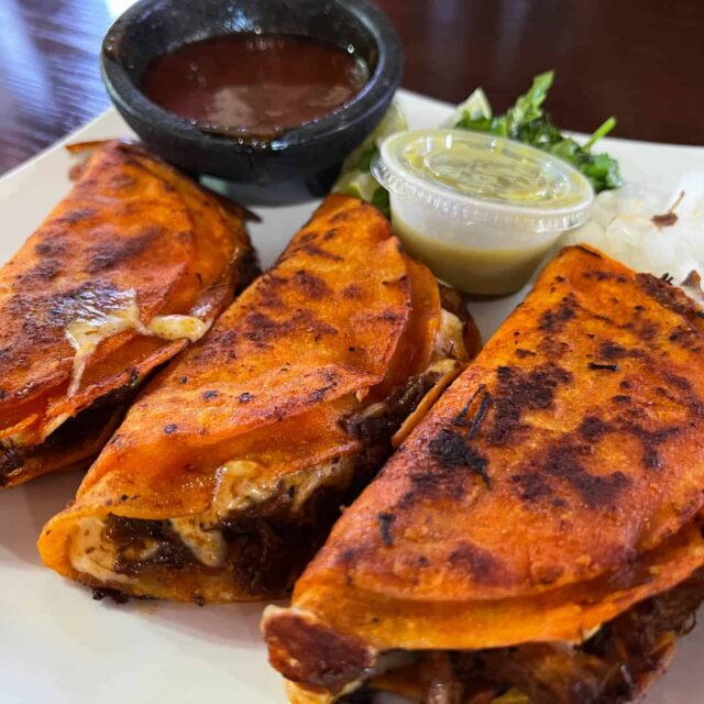 Three quesadillas on a plate with dipping sauce.