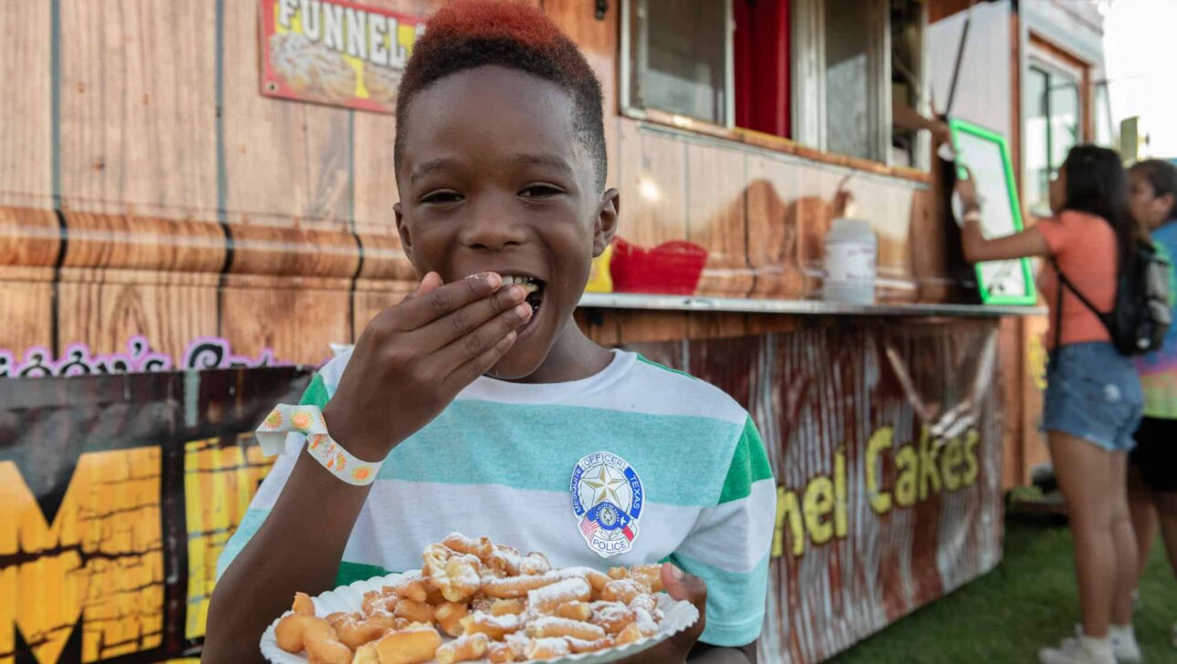 A young boy holding a plate of food in front of a food truck.