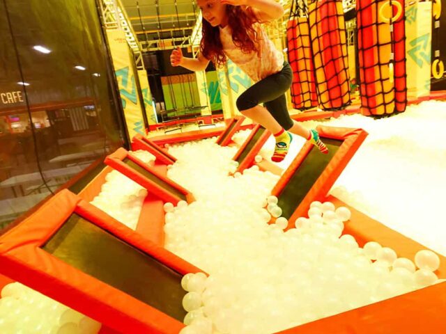 A girl is jumping on a trampoline in an indoor playground.