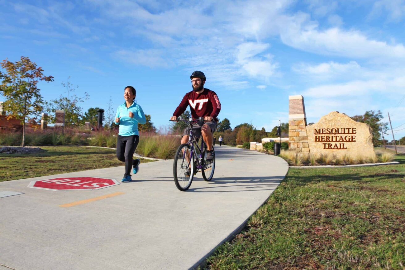 Two people riding bikes on a sidewalk.