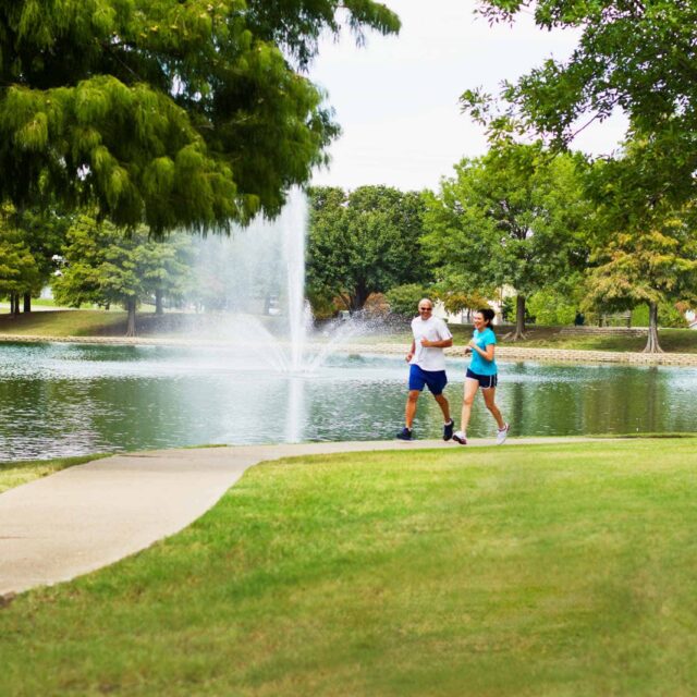 A man and woman jogging along a path near a pond.