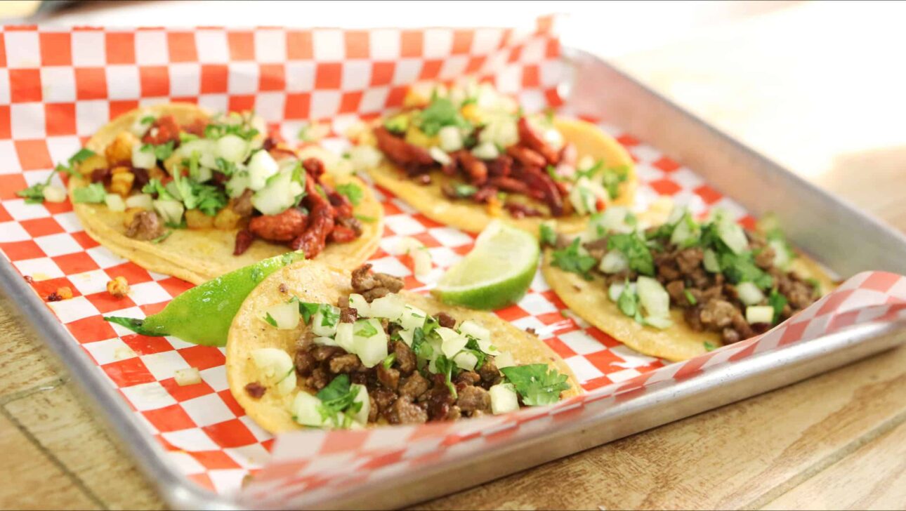 Four tacos on a tray on a wooden table.