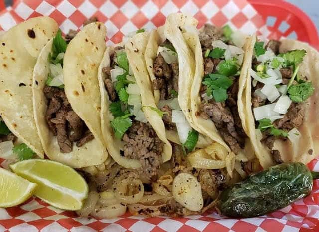 Four tacos are sitting in a basket with lime wedges.