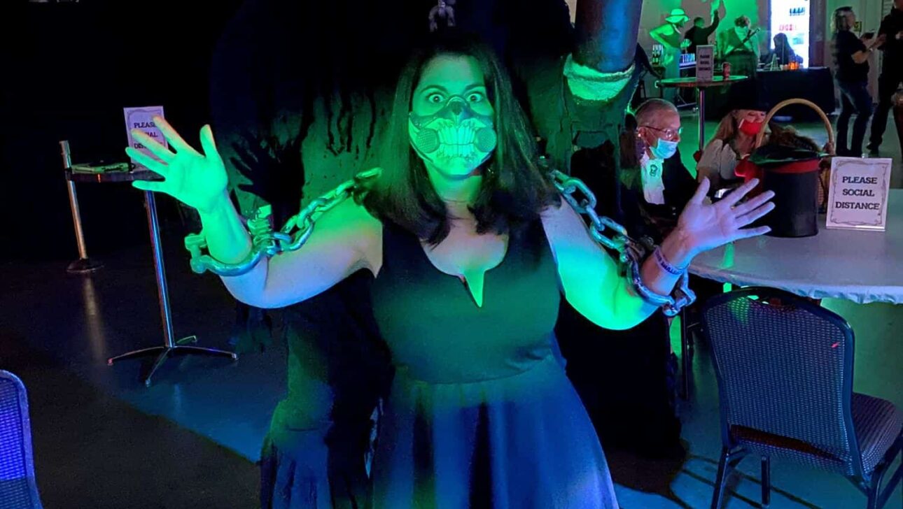 A person in a horror monster costume posing with another person at a themed event with green lighting in the background.