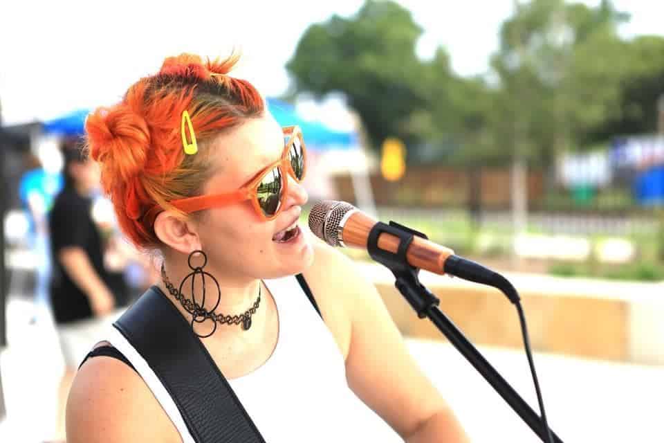 A woman with orange hair singing into a microphone.