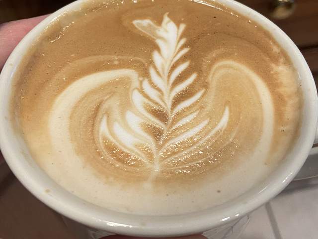 A close-up of a latte with intricate leaf-like latte art on its foamy surface in a white cup.