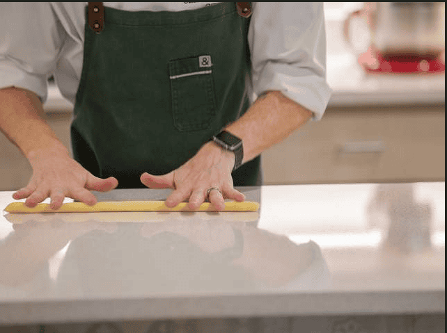 Person in a green apron rolling dough on a kitchen counter.