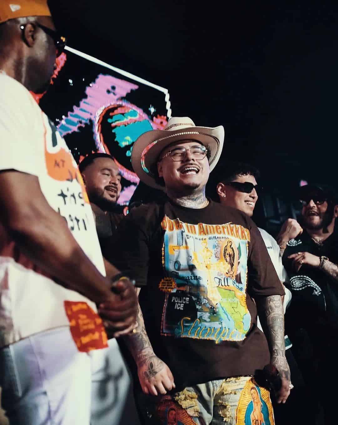 Group of people standing together, one wearing a cowboy hat and graphic T-shirt, smiling, with a colorful background behind them.