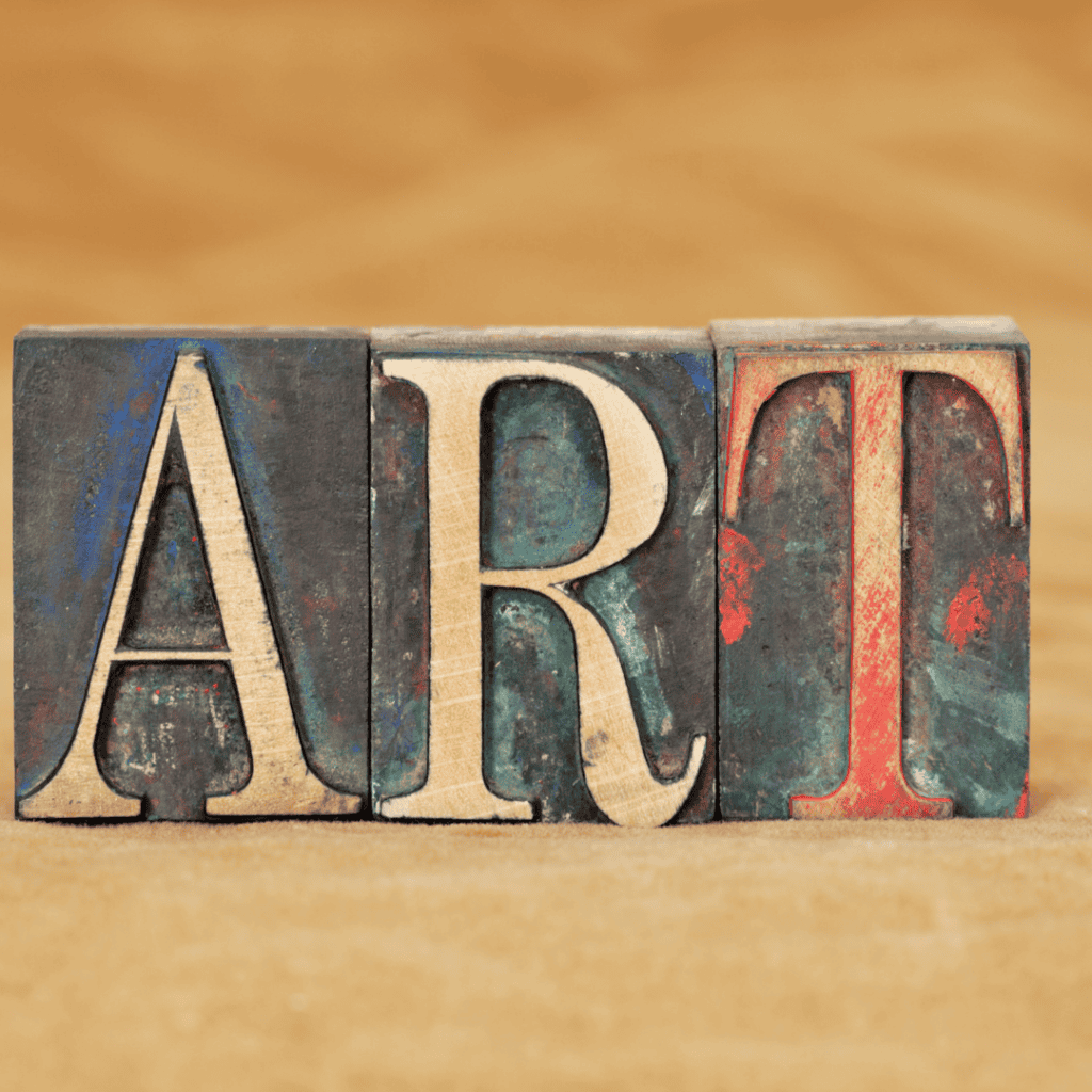 Wooden blocks with the letters A, R, T arranged to spell "ART" against a blurred brown background.