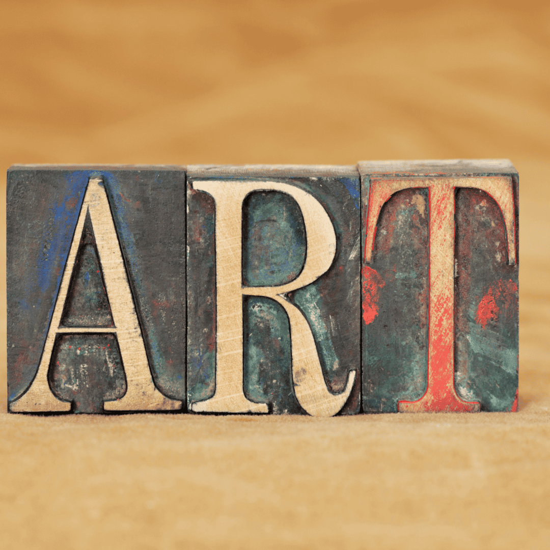 Wooden blocks with the letters A, R, T arranged to spell "ART" against a blurred brown background.