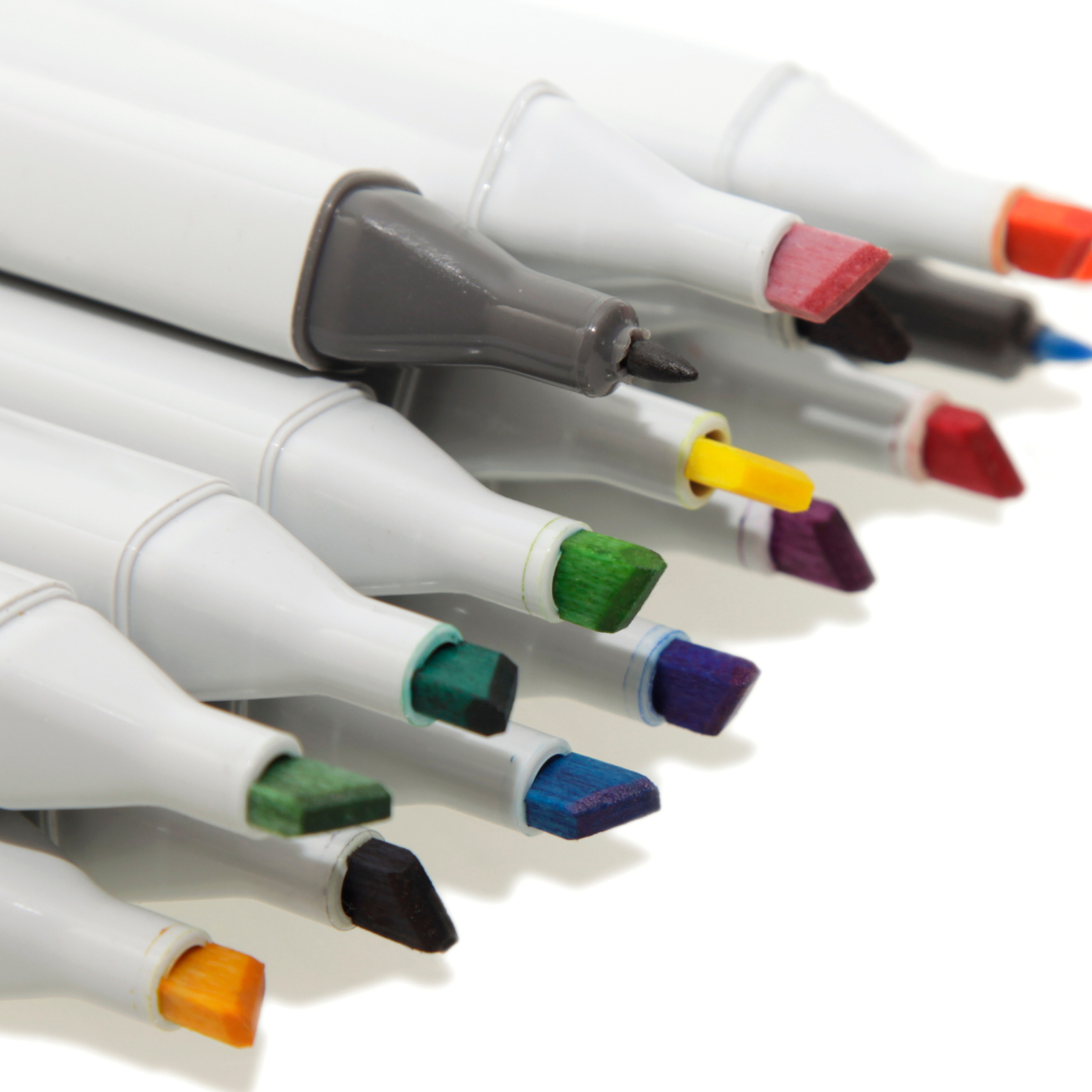 A close-up of the tips of various colored markers arranged in a row on a white surface.